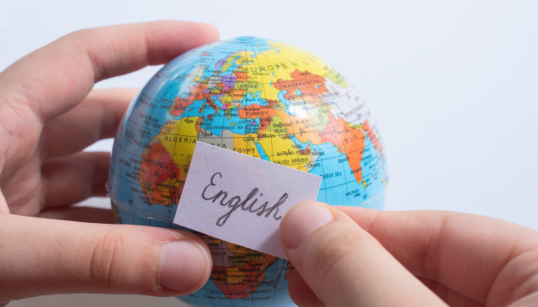 Showing English as a Global Linga Franca as a person is putting the world English on top of a globe. 