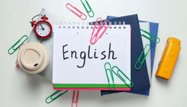 "English" written on a notebook with paper clips and coffee around it to learn english grammar